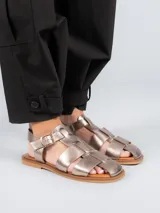 Sandalias bajas doradas con diseño de tiras entrecruzadas y hebilla lateral.