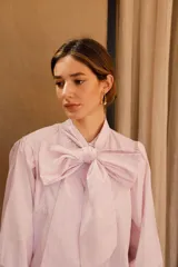 Camisa de algodón a rayas verticales rosas y blancas, con cuello alto y lazo grande en el cuello.