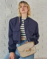 Bandolera color beige con textura símil reptil, cierre con broche metálico dorado y correa larga regulable.