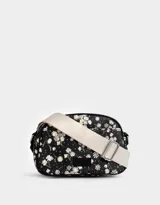 Bandolera negra con estampado de flores blancas, correa de algodón ajustable y cierre superior.