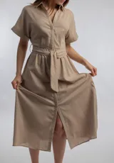 Vestido camisero midi color beige, con cuello camisero, mangas cortas con dobladillo, cierre frontal con botones y lazo para ajustar en la cintura.