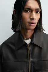 Cazadora estilo bomber cropped fit de piel negra, con cuello solapa, cierre frontal de cremallera, bolsillos frontales de plastrón con solapa y puños y bajo de rib elástico ancho.