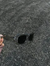 Gafas de sol rectangulares con montura transparente gris y lentes negras.