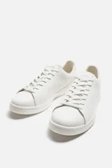 Zapatillas urbanas de cuero liso color blanco, con cordones y suela plana.