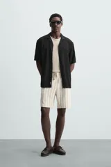 Camisa de calce relajado confeccionada en tejido fluido de mezcla de viscosa, color blanco. Presenta cuello bowling, manga corta, aberturas laterales en el bajo y cierre frontal con botones al tono.