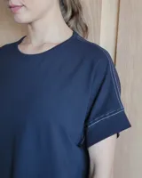 Vestido largo color crudo con cuello redondo y mangas cortas con ribete negro. Tiene corte recto y aberturas laterales en el ruedo.