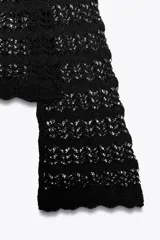 Jersey corto de punto calado negro, con cuello redondo amplio y mangas largas acampanadas.