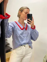 Camisa de algodón a cuadros azules y blancos con cuello y puños con volados rojos.