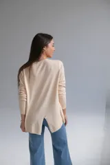 Sweater color beige de corte recto con cuello a la base. La parte delantera es más corta que la trasera y tiene una abertura en la parte baja de la espalda.