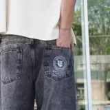 Pantalón de jean negro con lavado oscuro y efecto desgastado, de corte ultra ancho y tiro alto. Presenta un parche circular con logo en el bolsillo trasero derecho.
