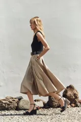 Vestido midi con cuerpo negro sin mangas y falda plisada color beige. Incluye cinturón negro con hebilla rectangular.