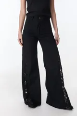 Pantalón de jean negro de pierna ancha con cortes en los laterales que van desde la pretina al bajo del pantalón. Por la mitad de la pierna presenta godets triangulares de encaje para darle mayor amplitud y detalles a la prenda.
