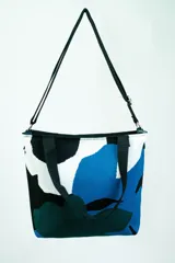Bolso tipo tote con estampado abstracto en tonos azul, blanco, negro y verde. Tiene doble asa de mano y correa larga regulable al hombro, ambas en color negro.