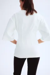 Remera larga color blanco de punto pesado de algodón, con escote barco, hombros caídos, mangas al codo y cintura entallada con pinzas acolchadas.