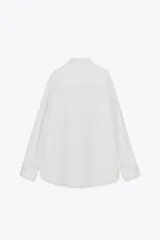 Camisa blanca con finas rayas verticales negras, de corte holgado, cuello solapa, manga larga con puños y bolsillo de plastrón en el pecho.