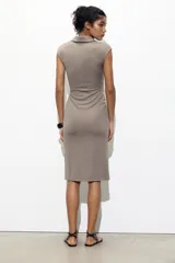 Vestido midi color gris topo, de cuello camisero y escote pico con manga corta. Tiene detalle de drapeado lateral y cierre frontal con botones metálicos.