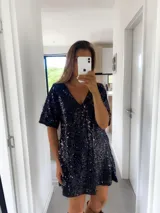Vestido corto negro con lentejuelas, escote en V y mangas cortas.