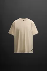Camiseta deportiva color beige confeccionada en tejido técnico ligero y elástico con estructura perforada, cuello redondo, manga corta, bajo asimétrico con aberturas laterales, acabados con costuras termofijadas y detalle de logo estampado. Zara Athleticz.