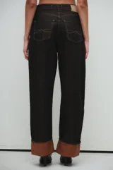 Pantalón de jean negro, corte recto y tiro medio/alto, con bolsillos clásicos y botamanga rebatida con interior color marrón.