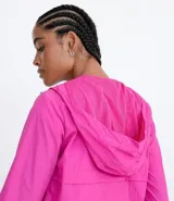 Campera rompeviento alargada color fucsia, con capucha, cierre frontal con cremallera color lila, bolsillos con solapa y puños elásticos.