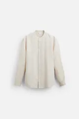 Camisa color beige claro, de corte relaxed fit, confeccionada en tejido de lino y algodón. Tiene cuello mao, manga larga con puños abotonados y cierre frontal con botones.