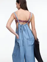 Mono largo de denim azul oscuro, con breteles finos regulables, escote recto, bolsillos traseros y corte amplio de pierna recta.