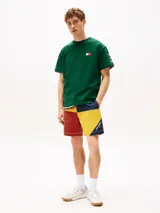 Remera verde de algodón con cuello redondo y corte amplio. Presenta el logo de Tommy Hilfiger en el pecho y un logo oversize en la parte trasera. Tiene mangas cortas con hombros caídos y un parche con logo en la manga.