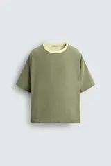 Camiseta color verde claro, de corte holgado, confeccionada en tejido de algodón con interior reversible de popelín. Tiene cuello redondo, manga corta y acabados con vivo combinado a contraste.