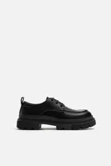 Zapato de vestir tipo blucher color negro, con detalle de bordón, tirador trasero y suela con volumen irregular.