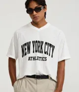 Remera de hombre con corte boxy, confeccionada en tejido mesh (malla) blanco, con cuello en V y estampa arqueada en negro que dice "NEW YORK CITY ATHLETICS".