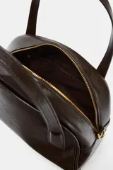 Bolso de mano y bandolera color marrón oscuro, con forma redondeada y doble asa superior. Presenta cierre principal de cremallera y un bolsillo interior con cierre.