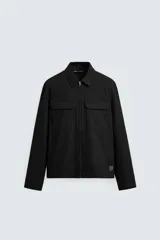 Sobrecamisa negra de corte relaxed fit confeccionada en tejido con mezcla de algodón. Tiene cuello solapa, manga larga con puños abotonados, bolsillos de plastrón con solapa en el pecho y laterales en la costura de la cadera. El cierre es frontal con cremallera.