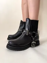 Botín negro de cuero vacuno con elásticos laterales y estribo desmontable con apliques y herrajes metálicos color níquel.