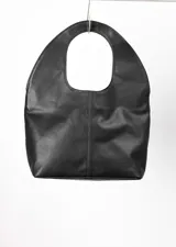 Bolso tote negro de cuero con manija circular rígida.