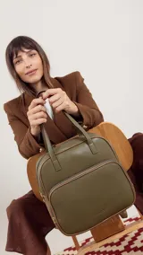 Mochila color marrón con doble asa de mano y correas traseras regulables. Presenta un bolsillo frontal con cierre y compartimento interno para iPad.