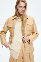 Camisa color crema de tejido fresco de mezcla de algodón, corte amplio, con cuello clásico, cierre frontal con botones, canesú en la espalda, hombros caídos, mangas largas con puños abotonados y bajo redondeado.