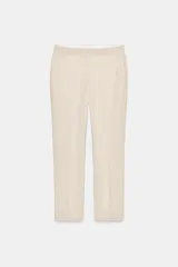 Pantalón tobillero color beige, de tiro medio, confeccionado en hilatura con algodón y lino. Presenta bolsillos laterales, raya planchada y cierre frontal con cremallera, botón y ganchos metálicos.