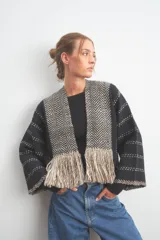 Chaqueta peplum tejida a rayas horizontales negras y grises, con mangas anchas y detalle de flecos en el ruedo.