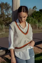 Chaleco tejido color crema con cuello en V y ribetes en naranja y negro. Diseño sin mangas y corte holgado. Ideal para usar sobre camisas o remeras de manga larga.