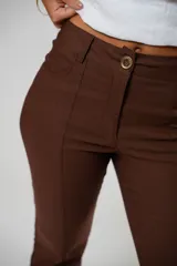 Pantalón marrón de tiro alto con cierre frontal de cremallera y botón. Tiene bolsillos delanteros y traseros, y corte acampanado.