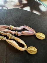 Collar con cinta de seda color beige y marrón, con cuentas doradas y medalla religiosa dorada.