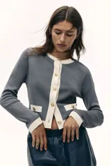 Cárdigan corto gris de punto fino con cuello redondo, cierre frontal con botones metálicos dorados y bolsillos decorativos con botón.