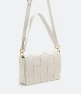 Bolso baguette mediano color blanco, con detalles a cuadros, doble correa (corta y transversal), cierre con botón a presión y textura tressé.