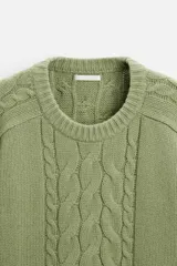 Sweater verde claro de punto con cuello redondo y mangas largas. Presenta diseño de trenzas en el centro y en las mangas.