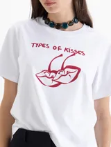 Remera blanca de manga corta con estampado frontal de dos cerezas con forma de labios y el texto "TYPES OF KISSES" en rojo.