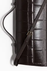 Cartera rectangular color marrón oscuro con efecto de piel de cocodrilo. Cuenta con un asa superior, solapa con cierre magnético oculto y una correa fina ajustable para llevar al hombro o cruzada. Interior forrado.