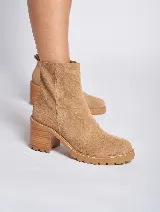 Bota corta de gamuza color marrón, con taco cuadrado de madera y suela track. Presenta un tirador en la parte posterior. Confeccionada 100% en cuero genuino.