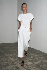 Camiseta blanca de algodón con cuello redondo, manga corta con dobladillo y dos bolsillos de parche en el frente con detalle de aplicación metálica.