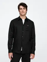 Camisa de manga larga color negro, confeccionada en lino, con cuello clásico y bolsillo de parche en el pecho con un pequeño bordado de oso.