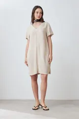 Vestido corto color beige melange, de lino, con cuello en V y mangas cortas. Presenta pespuntes verticales en contraste.